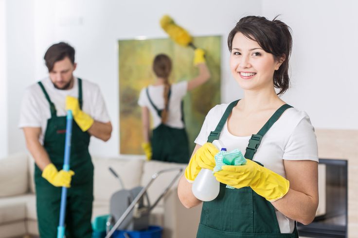 Three individuals wearing matching cleaning attire and gloves are actively cleaning a room